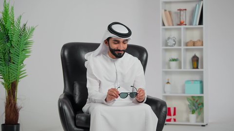 مفهوم القوة والرجولة والوسامة، الاهتمام بالأناقة والمظهر الخارجي، رجل عربي خليجي اماراتي يرتدي الكندورة و الغتره يجلس على كرسي يرتدي النظارات الشمسية، تعابير الفرح والسرور، ايماءات الثقة بالنفس
