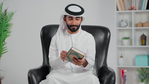 الإجتهاد و الخشوع في العباده، قراءة وتلاوة كتاب الله تعالى ,رجل عربي خليجي اماراتي يرتدي الكندورة و الغتره يمسك بيديه القرآن الكريم، التقرب الى رب العالمين ، أجواء روحانية دينية