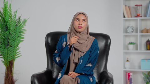 التركيز لإيجاد حل لمشكلة، امرأة عربية خليجية سعودية ترتدي العباءة والحجاب تجلس على كرسي تضع يديها على ذقنها بتعابير التفكير والتركيز بشيء ما، ايماءات شرود الذهن والحيرة والقلق، التأمل و التخطيط للمستقبل