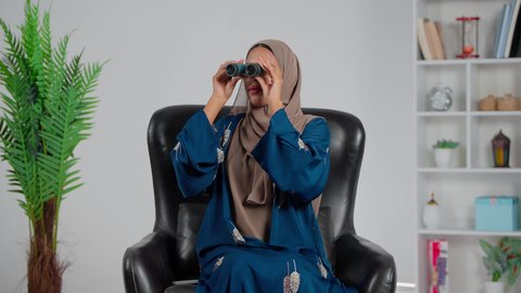 التخطيط المستقبلي للأهداف و الطموحات، رؤية الاشياء البعيدة عبر التلسكوب، حب الاستكشاف والمغامرة، امرأة عربية خليجية سعودية ترتدي العباءة والحجاب تجلس على كرسي تنظر من خلال منظار ثنائي العينين