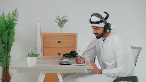 كتابة و تدوين الملاحظات، استخدام الهيدفون والتقنيات المتطورة في العمل، التواصل مع الزبائن لحل المشكلات والشكاوي، الاجابه على اسئلة العملاء، تصوير من الجانب موظف عربي خليجي سعودي يضع سماعة الرأس الصوتية يجلس امام الحاسب الالى يعمل في مجال خدمة العملاء ، اجراء اتصال من خلال جهاز الحاسوب