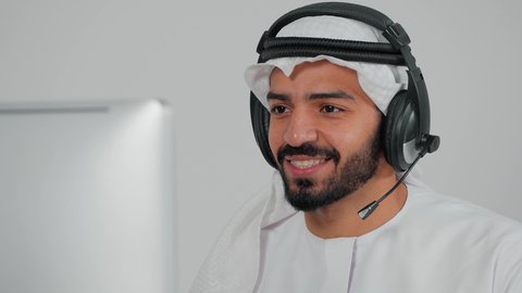 Communicating with customers to solve problems and complaints, answering customer questions, close-up of a Saudi Arabian Gulf employee wearing a headset sitting in front of a computer working in customer service, making a call via computer, using headphones and advanced technologies at work