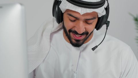 الاجابه على اسئلة العملاء، تصوير مقرب لموظف عربي خليجي سعودي يضع سماعة الرأس الصوتية  يجلس امام الحاسب الالى يعمل في مجال خدمة العملاء  ، اجراء اتصال من خلال جهاز الحاسوب، التواصل مع الزبائن لحل المشكلات والشكاوي، استخدام الهيدفون والتقنيات المتطورة في العمل