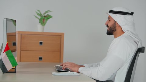 متابعة إستراتيجية العمل، مفهوم إدارة الأعمال، التفاهم والتعاون بين الزملاء لتحقيق أهداف الشركة، إنجاز المهام عبر الحاسب الالى، تصوير من الجانب لرجل عربي خليجي اماراتي يرتدي الكندورة و الغترة يجلس على كرسي متحرك يقوم باستلام اوراق العمل