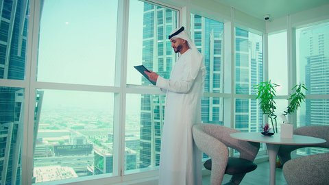 دراسة مشاريع جديدة، النمو الاقتصادي والاستثمار المالي،مفهوم إدارة الأعمال ، رجل عربي خليجي اماراتي يرتدي الكندورة والغترة ينظر من خلال الشرفة ، تحليل وتدقيق بيانات المشروع كتابه وتدوين الملاحظات