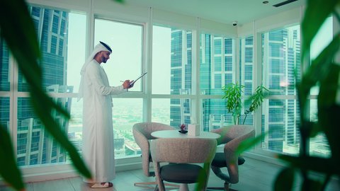 مفهم ادارة الاعمال  ،تحليل وتدقيق بيانات المشروع ،    رجل عربي خليجي اماراتي يرتدي الكندورة والغترة ينظر من خلال الشرفة ، ، كتابه وتدوين الملاحظات، دراسة مشاريع جديدة، النمو الاقتصادي والاستثمار المالي