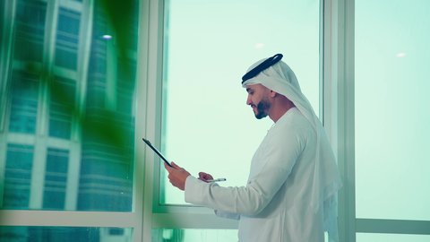 تحليل وتدقيق بيانات المشروع ،  رجل عربي خليجي اماراتي يرتدي الكندورة والغترة ينظر من خلال الشرفة ، ، كتابه وتدوين الملاحظات، دراسة مشاريع جديدة، النمو الاقتصادي والاستثمار المالي،مفهوم إدارة الأعمال