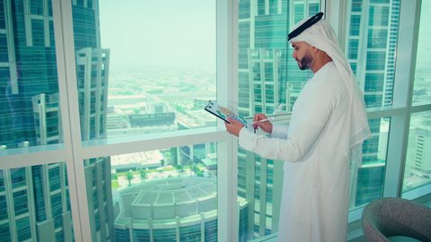 كتابه وتدوين الملاحظات، دراسة مشاريع جديدة، النمو الاقتصادي والاستثمار المالي،مفهوم إدارة الأعمال ، رجل عربي خليجي اماراتي يرتدي الكندورة والغترة ينظر من خلال الشرفة ، تحليل وتدقيق بيانات المشروع