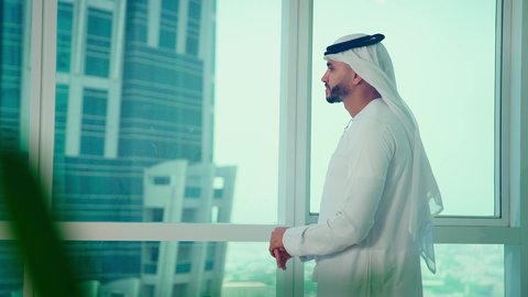 دراسة مشاريع جديدة، النمو الاقتصادي والاستثمار المالي،مفهوم إدارة الأعمال ، رجل عربي خليجي اماراتي يرتدي الكندورة والغترة ينظر من خلال الشرفة ، تحليل وتدقيق بيانات المشروع كتابه وتدوين الملاحظات