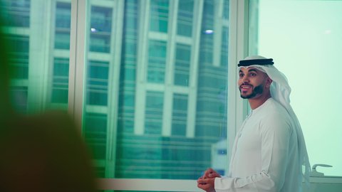 النمو الاقتصادي والاستثمار المالي، دراسة مشاريع جديدة، مفهوم إدارة الأعمال ، رجل عربي خليجي اماراتي يرتدي الكندورة والغترة ينظر من خلال الشرفة ، تحليل وتدقيق بيانات المشروع كتابه وتدوين الملاحظات