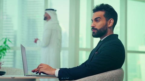 Emirati man wearing formal suit making a video call via laptop, business management concept, auditing and analyzing project data, economic growth and financial investment, studying new projects, using modern technologies, completing tasks through laptop, Emirati young man wearing kandura and ghutra making a phone call via mobile