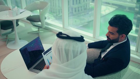 دراسة مشاريع جديدة، النمو الاقتصادي والاستثمار المالي ، صعود وهبوط البورصة، متابعة مخطط الرسم البياني، تدقيق وتحليل بيانات المشروع،احتماع زملاء عمل فى مقر عملهم احدهما يرتدي البدلة الرسمية يقومون بتحليل البيانات على الحاسوب المحمول