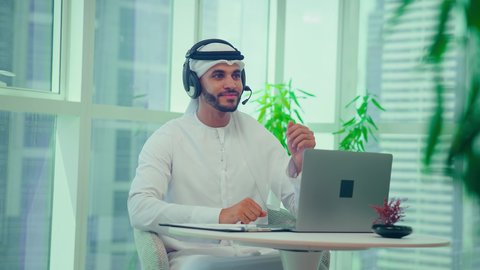 مفهوم إدارة الأعمال، تدقيق وتحليل بيانات المشروع، تدوين وكتابة الملاحظات، إنجاز المهام من خلال اللابتوب ، دراسة مشاريع جديدة، إستخدام تقنيات حديثة، رجل اماراتي يرتدي الكندورة والغترة وسماعات الرأس يقوم باجراء مكالمة فيديو عبر جهاز الحاسوب المحمول، النمو الاقتصادي والاستثمار المالي