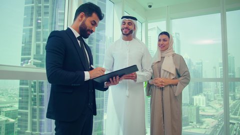 Business management concept, completing tasks using a laptop, studying new projects, using modern technologies, meeting of Arab Gulf and Emirati colleagues with a man wearing a formal suit to analyze and audit the project via a laptop, economic growth and financial investment