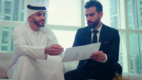 رجل اعمال عربي اماراتي خليجي يرتدي الكندورة والغترة يتناقش مع عميل يرتدي البدلة الرسمية، اتفاقية عمل لمشروع جديد، تحليل وتخطيط المشاريع، تطوير العمل وحل المشكلات، الوحدة والعمل الجماعي، تحقيق اهداف الشركه