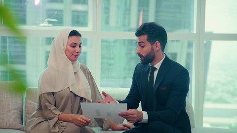 Unity and teamwork, project analysis and planning, business agreement for a new project, an Emirati Gulf Arab woman wearing an abaya and hijab discussing with a client wearing a suit, business development and problem solving, achieving company goals