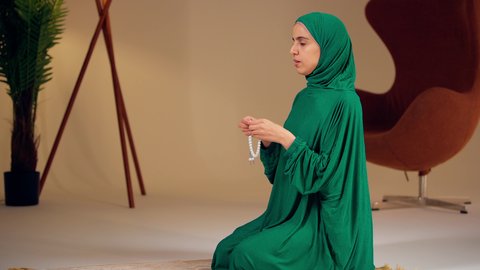 امراه عربيه خليجيه اماراتيه ترتدي العباءه والحجاب تمسك بيدها سبحة من حبات من الخرز البيضاء ، مفهوم التسبيح والتهليل ،سيدة سعودية تقوم بذكر الله تعالى، العبادة والطاعة والتقرب الى الله،الاجتهاد في العبادات