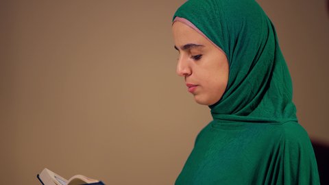 The concept of reflecting on the verses and chapters of the Holy Quran, striving in worship, reading, memorizing, and perfecting the Book of God, reciting the noble Quran, an Arab Gulf woman from the UAE wearing an abaya and hijab holding the Quran in her hand, a Saudi woman engaged in the remembrance of God Almighty.