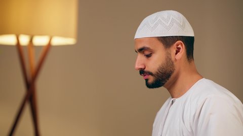 اجواء روحانية رمضانية، التقرب الى الله ،مفهوم أركان الاسلام والأيمان، الحفاظ على إقامة الصلوات الخمس بوقتها، الإجتهاد في العبادة، شاب عربي خليجي اماراتي يرتدي الثوب الأبيض والطاقية يقوم بأداء فريضة الصلاة، الشعور بالخشوع والطمأنينة