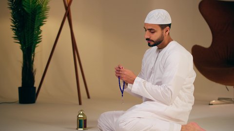 التسبيح والتهليل وذكر الله تعالى، العبادة والطاعة والتقرب الى الله، تصوير مقرب ليد شاب عربي خليجي اماراتي يرتدي الثوب الأبيض يمسك بيده سبحة من حبات من الخرز الزرقاء ، الاجتهاد في العبادات