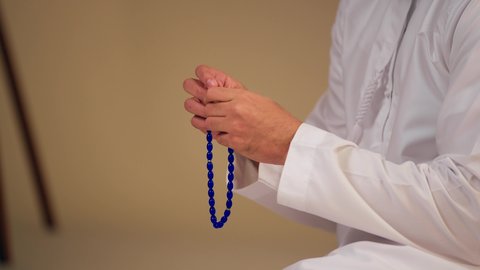 الاجتهاد في العبادات، تصوير مقرب ليد شاب عربي خليجي اماراتي يرتدي الثوب الأبيض يمسك بيده سبحة من حبات من الخرز الزرقاء ، التسبيح والتهليل وذكر الله تعالى،العبادة والطاعة والتقرب الى الله