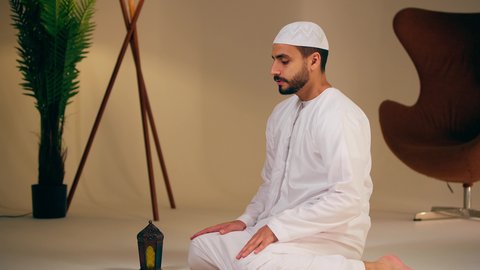 اجواء روحانية رمضانية، التقرب الى الله ،مفهوم أركان الاسلام والأيمان، الحفاظ على إقامة الصلوات الخمس بوقتها، الإجتهاد في العبادة، شاب عربي خليجي اماراتي يرتدي الثوب الأبيض والطاقية يقوم بأداء فريضة الصلاة، الشعور بالخشوع والطمأنينة