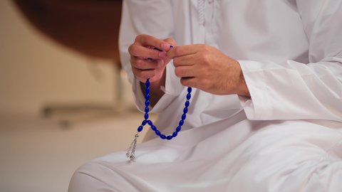 العبادة والطاعة والتقرب الى الله، تصوير مقرب ليد شاب عربي خليجي اماراتي يرتدي الثوب الأبيض يمسك بيده سبحة من حبات من الخرز الزرقاء ، التسبيح والتهليل وذكر الله تعالى، الاجتهاد في العبادات