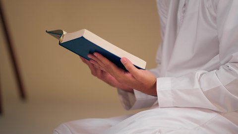 تصوير مقرب لشاب عربي خليجي اماراتي يرتدي الثوب الأبيض والطاقية يحمل بيده القرآن، مفهوم الاجتهاد في العبادة، قراءة كتاب الله وحفظه وتجويده، تلاوة المصحف الشريف، شاب عربي خليجي اماراتي يرتدي الثوب الأبيض والطاقية يحمل بيده القرآن
