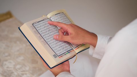 مفهوم الاجتهاد في العبادة، تصوير مقرب لشاب عربي خليجي اماراتي يرتدي الثوب الأبيض والطاقية يحمل بيده القرآن،  قراءة كتاب الله وحفظه وتجويده، تلاوة المصحف الشريف، شاب عربي خليجي اماراتي يرتدي الثوب الأبيض والطاقية يحمل بيده القرآن