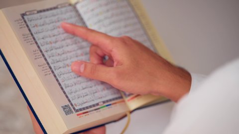 تصوير مقرب لشاب عربي خليجي اماراتي يرتدي الثوب الأبيض والطاقية يحمل بيده القرآن، مفهوم الاجتهاد في العبادة، قراءة كتاب الله وحفظه وتجويده، تلاوة المصحف الشريف، شاب عربي خليجي اماراتي يرتدي الثوب الأبيض والطاقية يحمل بيده القرآن