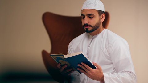 مفهوم الاجتهاد في العبادة، قراءة كتاب الله وحفظه وتجويده، تلاوة المصحف الشريف، شاب عربي خليجي اماراتي يرتدي الثوب الأبيض والطاقية يحمل بيده القرآن