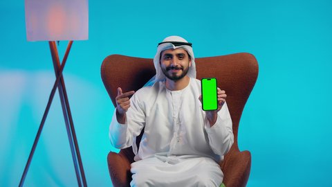 استخدام الهاتف المحمول، إجراء بث مباشر مع الأهل والأصدقاء، الاشارة الى شاشة خضراء كروما ، تصفح مواقع التواصل الاجتماعي ، رجل عربي خليجي اماراتي يرتدي الكندورة والغتره يمسك الجوال بيده ، دمج التقنيات الحديثة فى الحياة اليومية