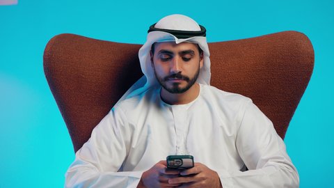 تصفح مواقع التواصل الاجتماعي ،  رجل عربي خليجي اماراتي يرتدي الكندورة والغتره  يمسك الجوال بيده ، دمج التقنيات الحديثة فى الحياة اليومية ، استخدام الهاتف المحمول ، إجراء بث مباشر مع الأهل والأصدقاء، التقاط صور السيلفي التذكارية