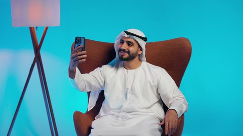 إجراء بث مباشر مع الأهل والأصدقاء، تصفح مواقع التواصل الاجتماعي ،  رجل عربي خليجي اماراتي يرتدي الكندورة والغتره  يمسك الجوال بيده ، دمج التقنيات الحديثة فى الحياة اليومية ، استخدام الهاتف المحمول ،  التقاط صور السيلفي التذكارية