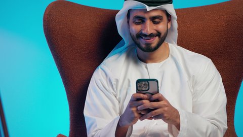 دمج التقنيات الحديثة فى الحياة اليومية ،تصفح مواقع التواصل الاجتماعي ،  رجل عربي خليجي اماراتي يرتدي الكندورة والغتره  يمسك الجوال بيده ،  استخدام الهاتف المحمول ، إجراء بث مباشر مع الأهل والأصدقاء، التقاط صور السيلفي التذكارية