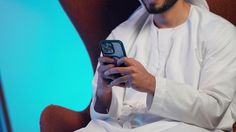تصفح مواقع التواصل الاجتماعي ،  رجل عربي خليجي اماراتي يرتدي الكندورة والغتره  يمسك الجوال بيده ، دمج التقنيات الحديثة فى الحياة اليومية ، استخدام الهاتف المحمول ، إجراء بث مباشر مع الأهل والأصدقاء، التقاط صور السيلفي التذكارية