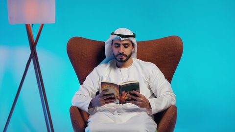 مطالعة القصص التصويرية المسلية, تمضية أوقات الفراغ بالتعلم والتثقف الذاتي, إيماءات الانتباه والتركيز ,  رجل عربي خليجي اماراتي يرتدي الكندورة والغترة يقوم بالقراءة بتمعن, تنمية مهارات القراءة , الاهتمام بتصفح الكتب المفيدة