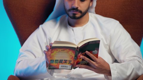 تمضية أوقات الفراغ بالتعلم والتثقف الذاتي, إيماءات الانتباه والتركيز ,  رجل عربي خليجي اماراتي يرتدي الكندورة والغترة يقوم بالقراءة بتمعن, مطالعة القصص التصويرية المسلية, تنمية مهارات القراءة , الاهتمام بتصفح الكتب المفيدة