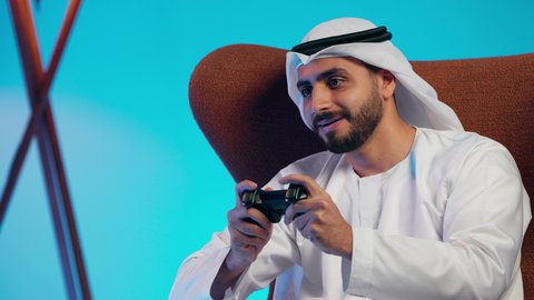 الاستمتاع بالانشطة الممتعه، التفاعل والاندماج مع ألعاب الفيديو، قضاء وقت ممتع ومسلي، استخدام اجهزة وتقنيات الكترونية ترفيهيه حديثة,  رجل عربي خليجي اماراتي يرتدي الكندورة والغتره يمسك بيده عصا التحكم