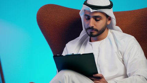 أوراق خاصة بالعمل, تدوين المهام اليومية ، رجل عربي خليجي اماراتي يرتدي الكندورة والغترة  يحمل بيديه اوراق بيضاء وقلم، شابه سعوديه تقوم بالبحث العلمي، قراءة الملاحظات والمعلومات ، متابعة الخطط والمشاريع