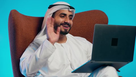 تعابير الترحيب والتعارف ،استخدام التقنيات الحديثة ، إجراء مكالمات الفيديو مع الأهل والأصدقاء، اجتماع عمل عن بعد، رجل عربي خليجي اماراتي يرتدي الكندورة والغتره وسماعات الرأس يمسك جهاز الحاسوب المحمول وينظر إليه بإيماءات السعادة