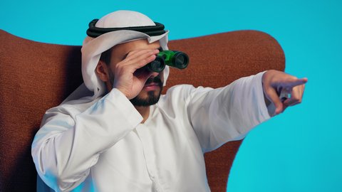 The use of binoculars to discover and bring distant things closer, an Emirati Gulf Arab man wearing a kandura and ghutrah sits on a comfortable chair holding binoculars in his hand and looking at something, a love for exploration and adventure, gestures of enjoyment and pleasure.