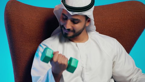 المحافظة على الصحة واللياقة الجسدية، ممارسة التمارين الرياضية مع الدمبل،تمارين رفع الأثقال (دمبلز)،  رجل عربي خليجي اماراتي يرتدي الكندورة والغتره  يقوم برفع الأوزان الحديدية الثقيلة