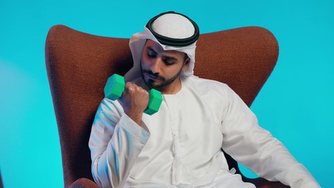 تمارين رفع الأثقال (دمبلز)،  ممارسة التمارين الرياضية مع الدمبل،رجل عربي خليجي اماراتي يرتدي الكندورة والغتره  يقوم برفع الأوزان الحديدية الثقيلة، المحافظة على الصحة واللياقة الجسدية
