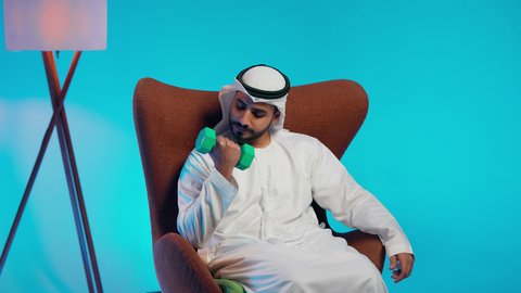 ممارسة التمارين الرياضية مع الدمبل،تمارين رفع الأثقال (دمبلز)،  رجل عربي خليجي اماراتي يرتدي الكندورة والغتره  يقوم برفع الأوزان الحديدية الثقيلة، المحافظة على الصحة واللياقة الجسدية