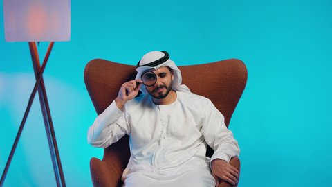 مفهوم توضيح الصورة، الفحص والاستكشاف والرؤية عن قرب، ايماءات السعادة والسرور،رجل عربي خليجي اماراتي يرتدي الكندورة والغترة ينظر من خلال العدسة المكبرة، التدقيق والتركيز باستخدام الأدوات البصرية