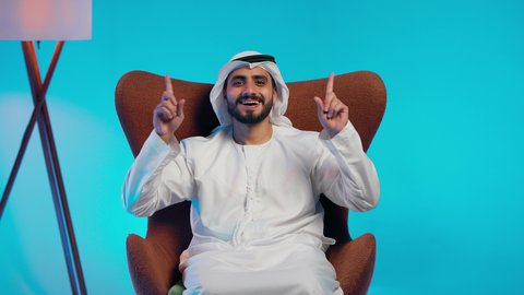 Movements indicating this place (here), indicating a specific location, identifying the place of a specific element, an Arab Gulf Emirati man wearing a kandura and ghutrah pointing with his index fingers upwards.