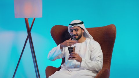 التعطر والتطيب بالبخور، استخدام خشب العود بالأعياد والمناسبات, العادات والتقاليد الاماراتيه ,  رجل عربي خليجي اماراتي يرتدي الكندورة والغتره يجلس على كرسي مريح يقوم بالتعطر من المبخرة, الاهتمام بالمظهر الخارجي والأناقة