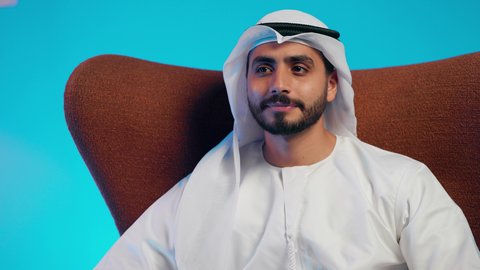 The need for sleep and the feeling of tiredness and lethargy, expressions of contemplation and thought, an Arab Gulf Emirati man wearing a kandura and ghutrah sitting on a comfortable chair with his hands behind his head in gestures of comfort and relaxation.