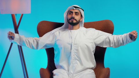 تعابير التأمل والتفكير، رجل عربي خليجي اماراتي يرتدي الكندورة والغتره يجلس على كرسي مريح يضع يديه خلف راسه بإيماءات الراحة والإسترخاء،الحاجة إلى النوم والشعور بالتعب و الخمول